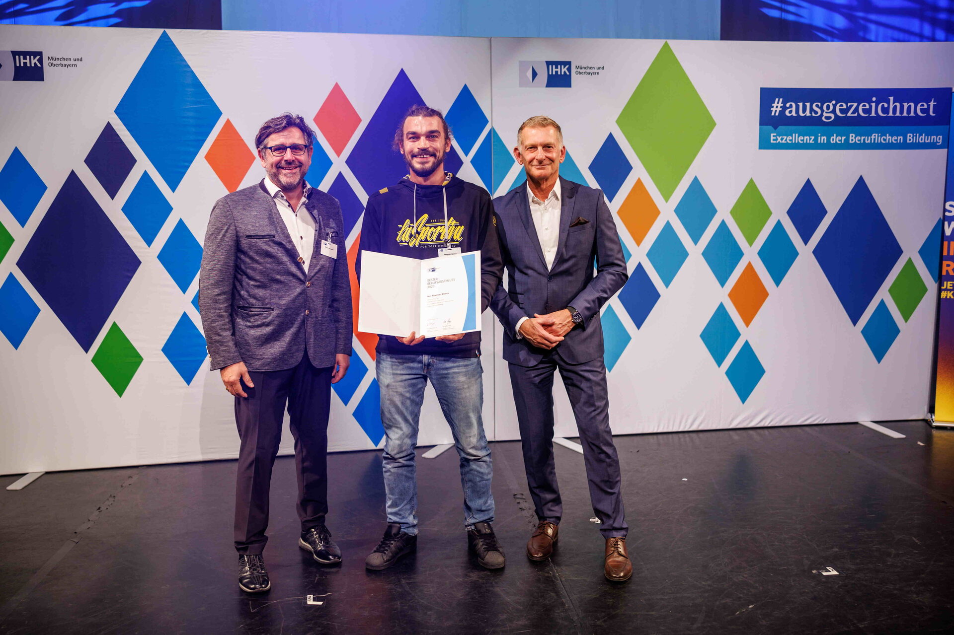 Hubert Schöffmann (re.), IHK-Bereichsleiter Berufliche Bildung, und Werner Mooseder, Vorsitzender des IHK-Regionalausschusses Dachau (stellvertretend für das IHK-Ehrenamt in der Region München), gratulieren Oberbayerns bestem Verkäufer am 26.10.2023 im Münchner GOP Varieté Theater