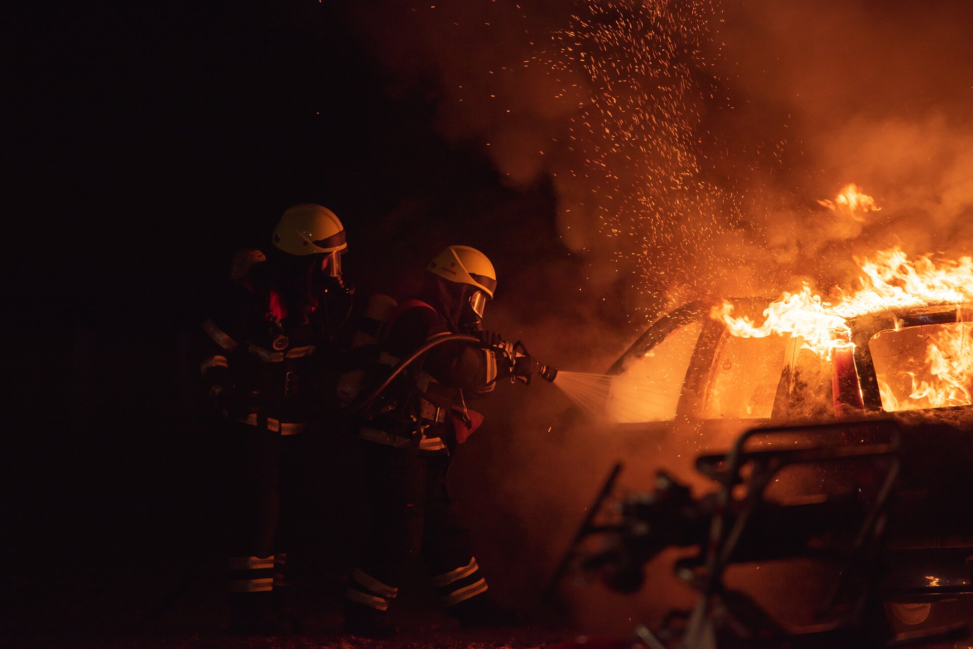 Two firefighters fighting a heavy car fire with water