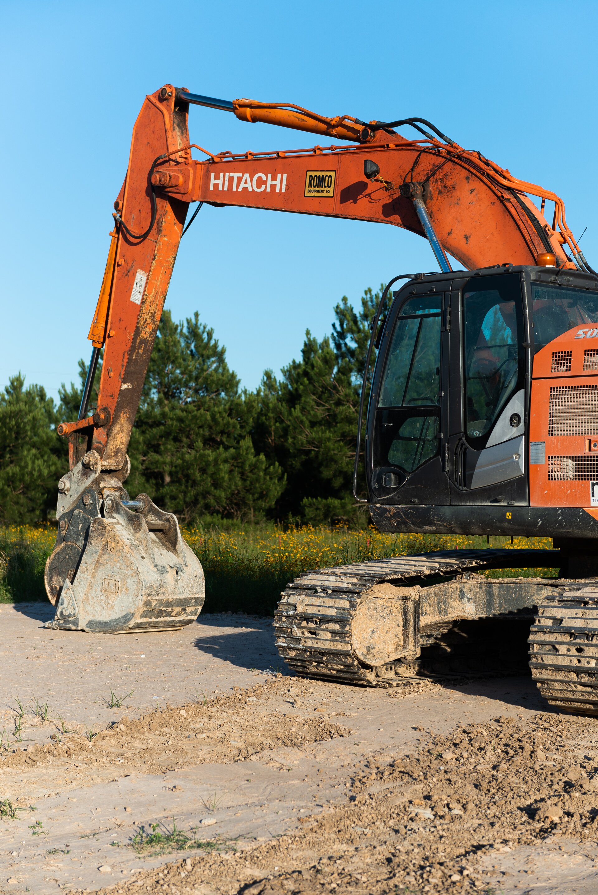 An excavator rests unused on a construction site during sunset.