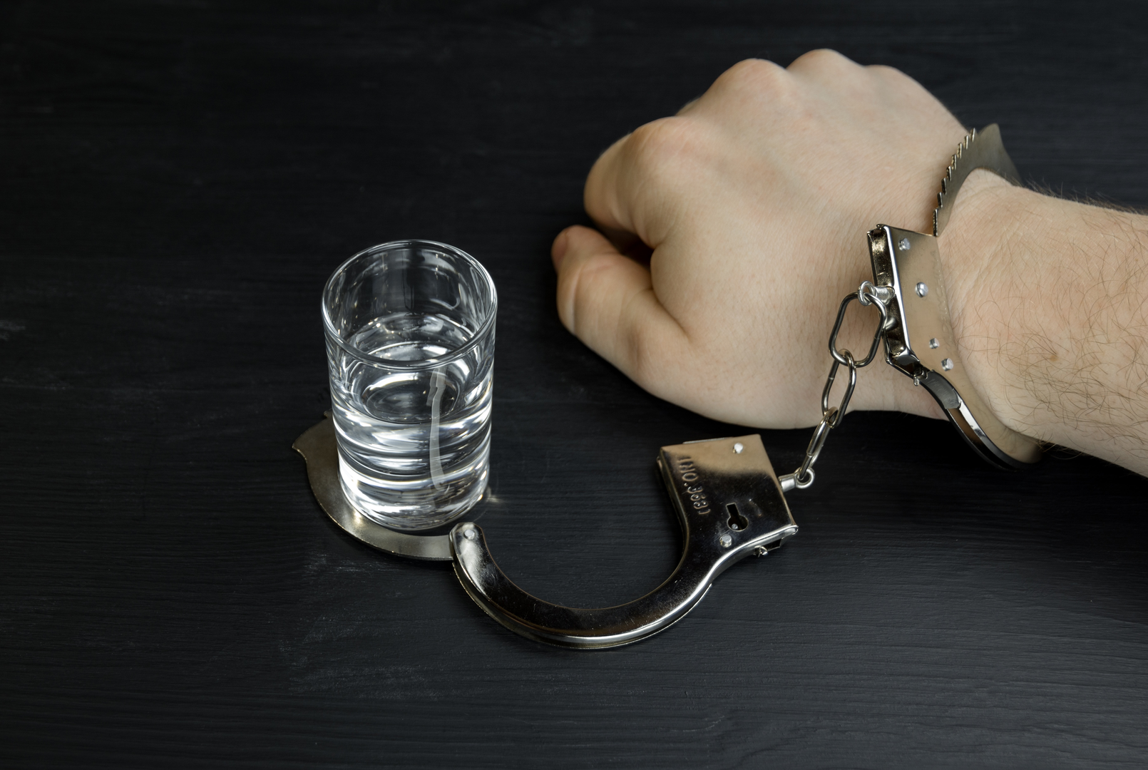 A man handcuffed to a glass of vodka. Alcohol addiction or alcoholism concept | © Unsplash / Bermix Studio