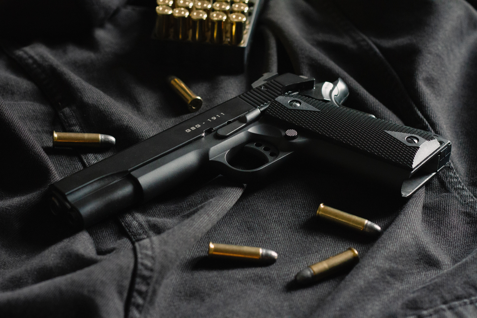 A black handgun on black cloth, with ammunition | © Unsplash / Tom Def