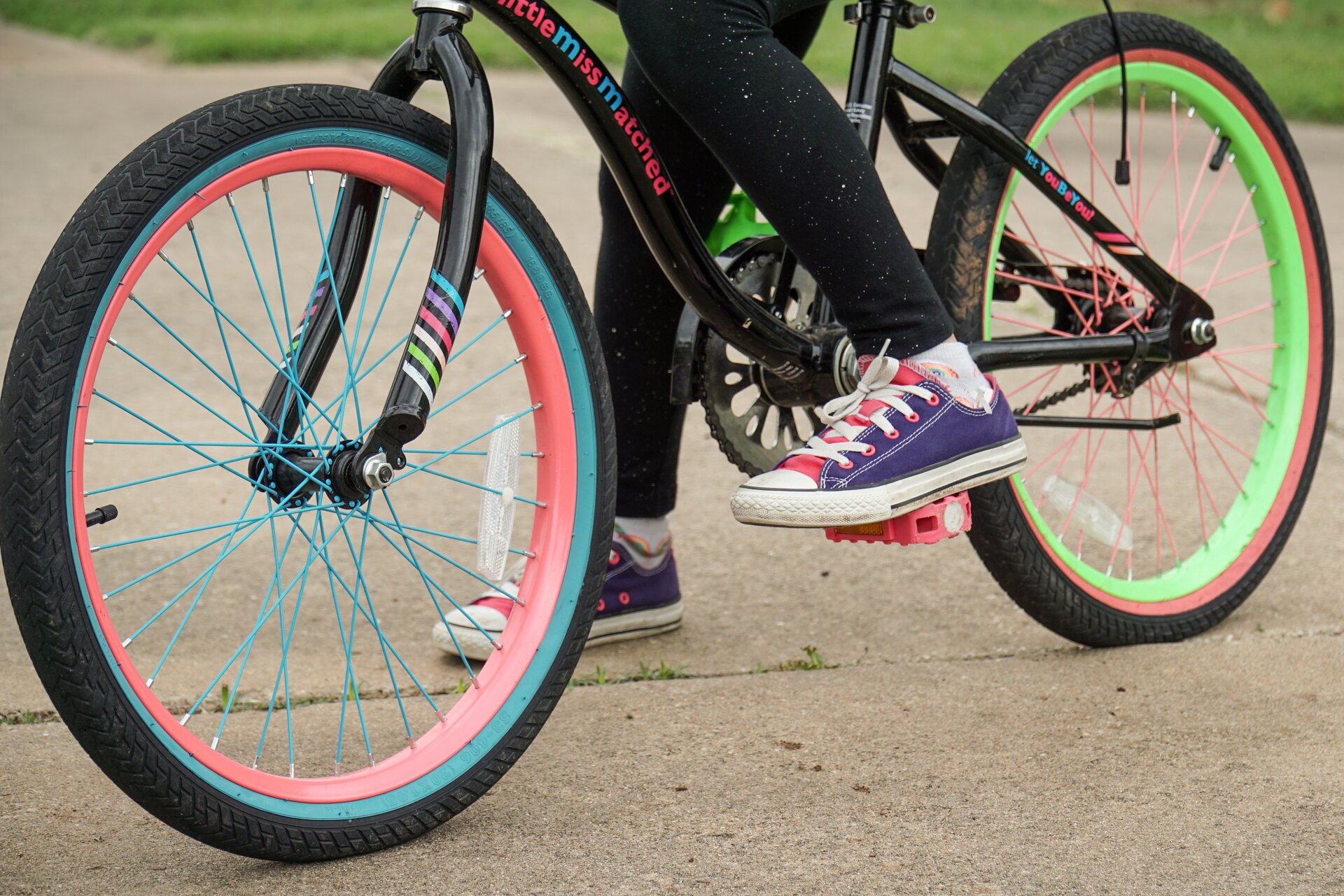Close up of young girl's bright colored converse shoes on top of a bright color kid's bike ready for a fun summer ride.