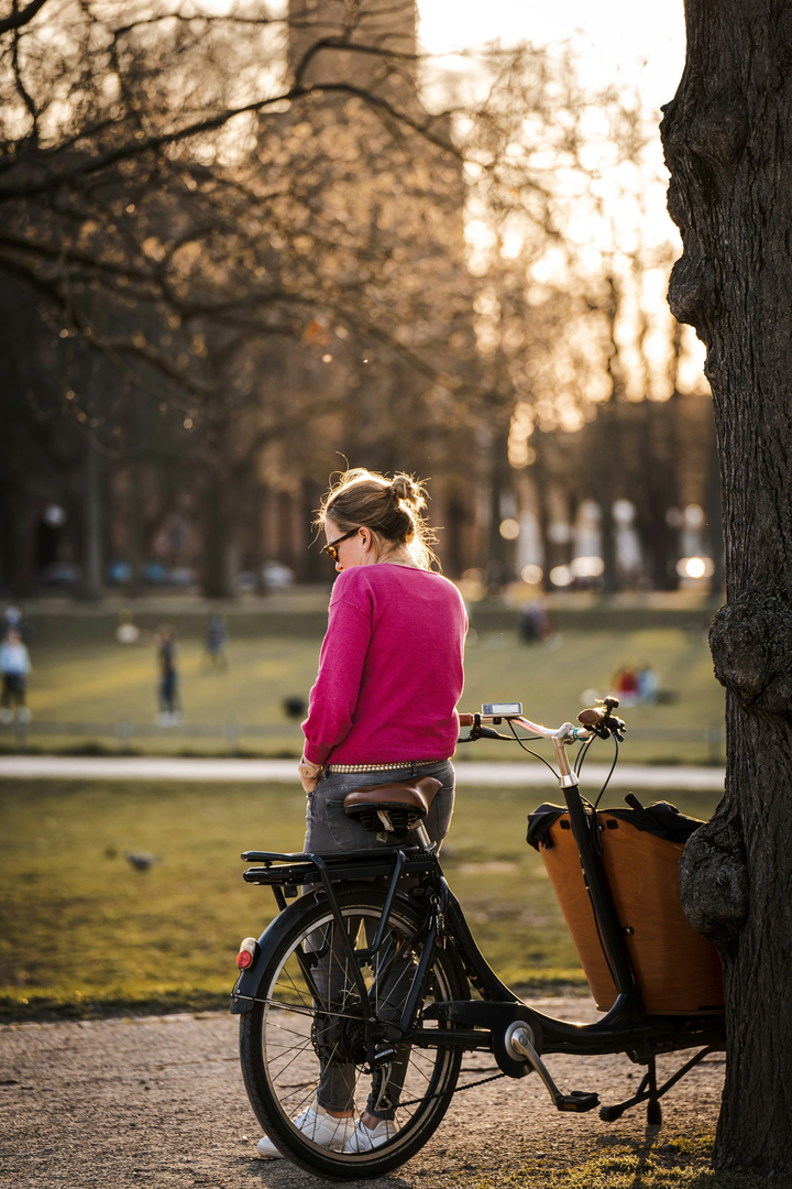 A woman using her phone right next to her cargo bike | © Unsplash / Mika Baumeister