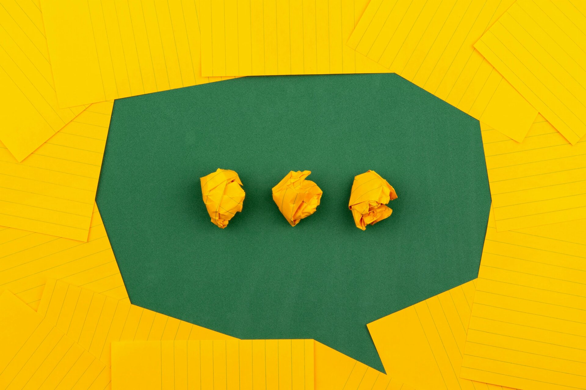 orange sheets of paper lie on a green school board and form a chat bubble with three crumpled papers.