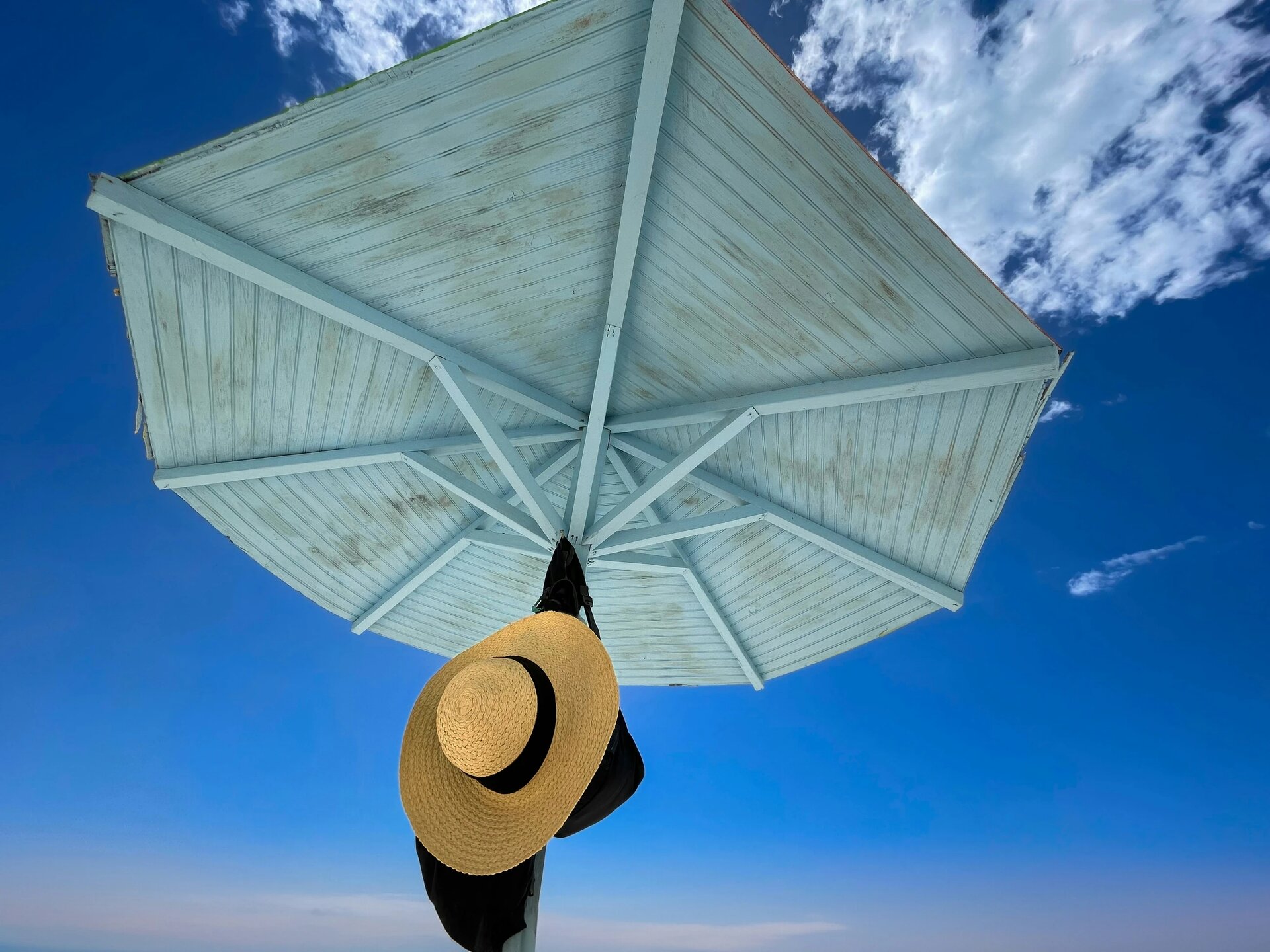 Relaxing in Antigua at Darkwood Beach looking up at a wooden beach umbrella against a blue sky with a single women's straw hat hung on a nail.