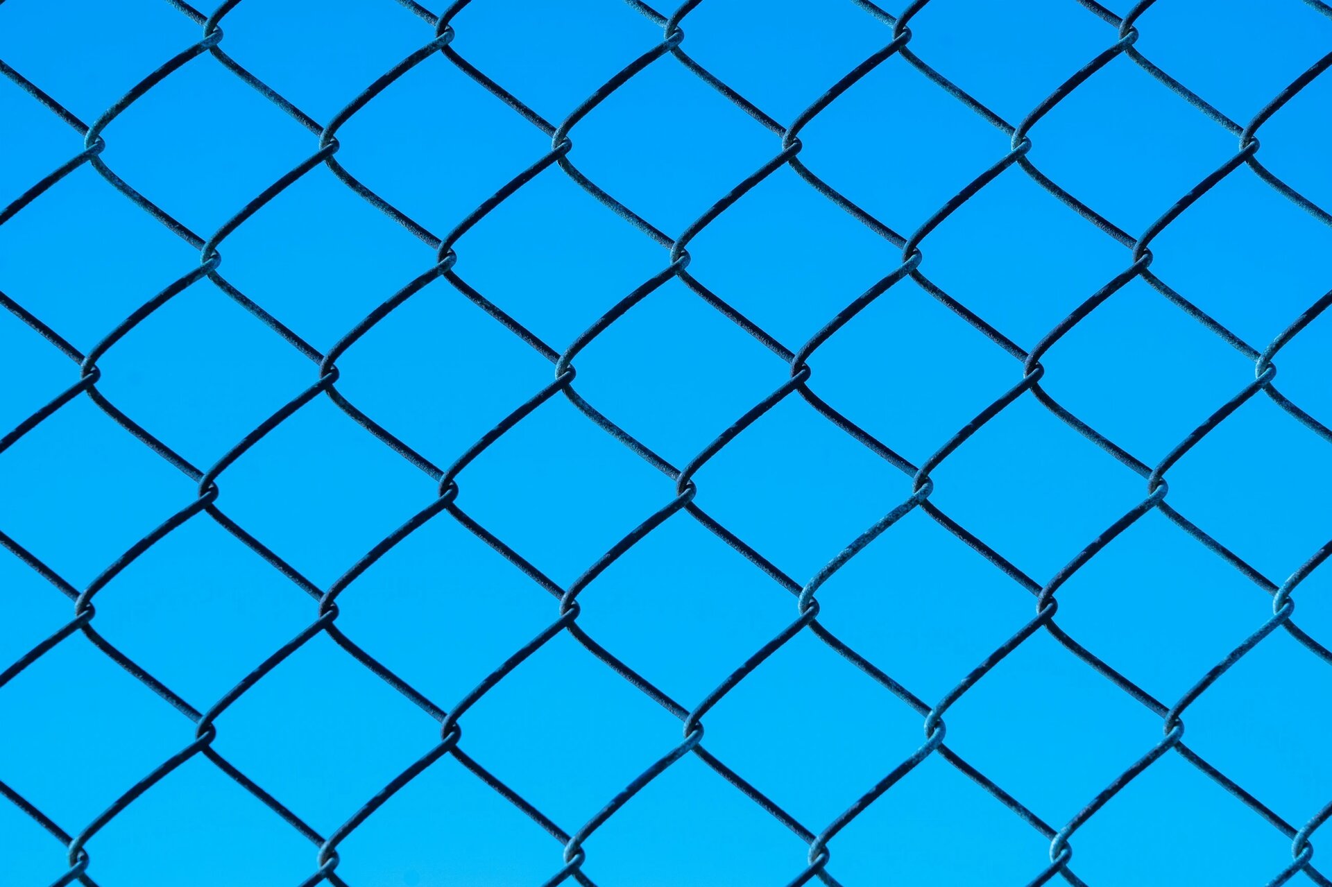 Metal chain link fence against a blue sky background.