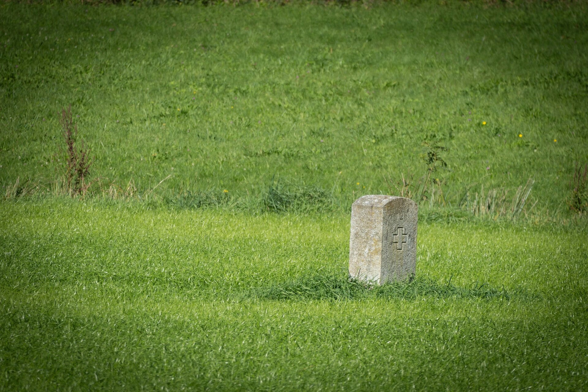 A modest stone marker etched with a cross stands in a peaceful green field, quietly signifying the border between France and Switzerland. Its simplicity contrasts with the deep historical and geographical significance it represents.