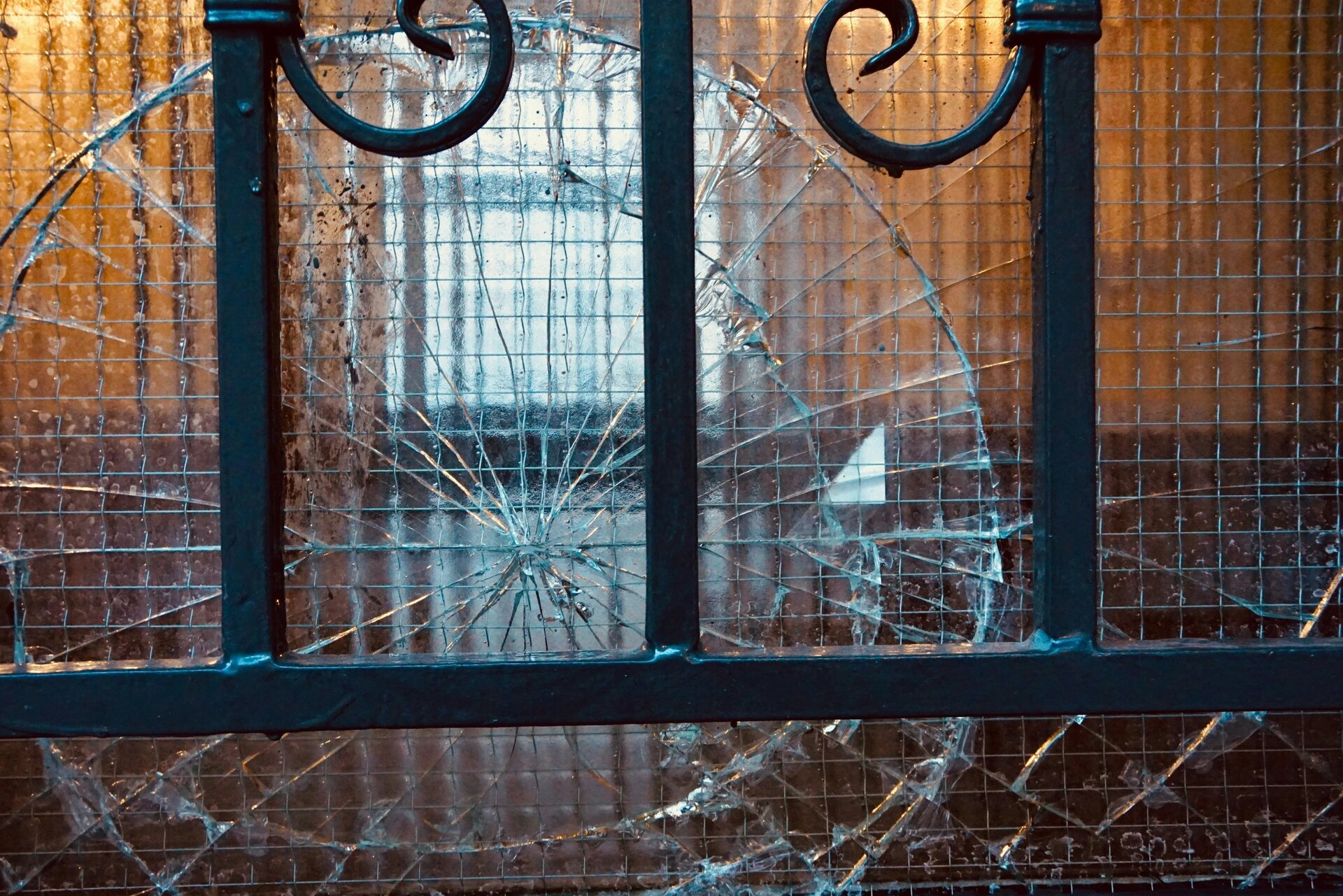 Shattered glass in an iron work door, circular pattern, into the light, warm soft oranges and blue reflections from glass.